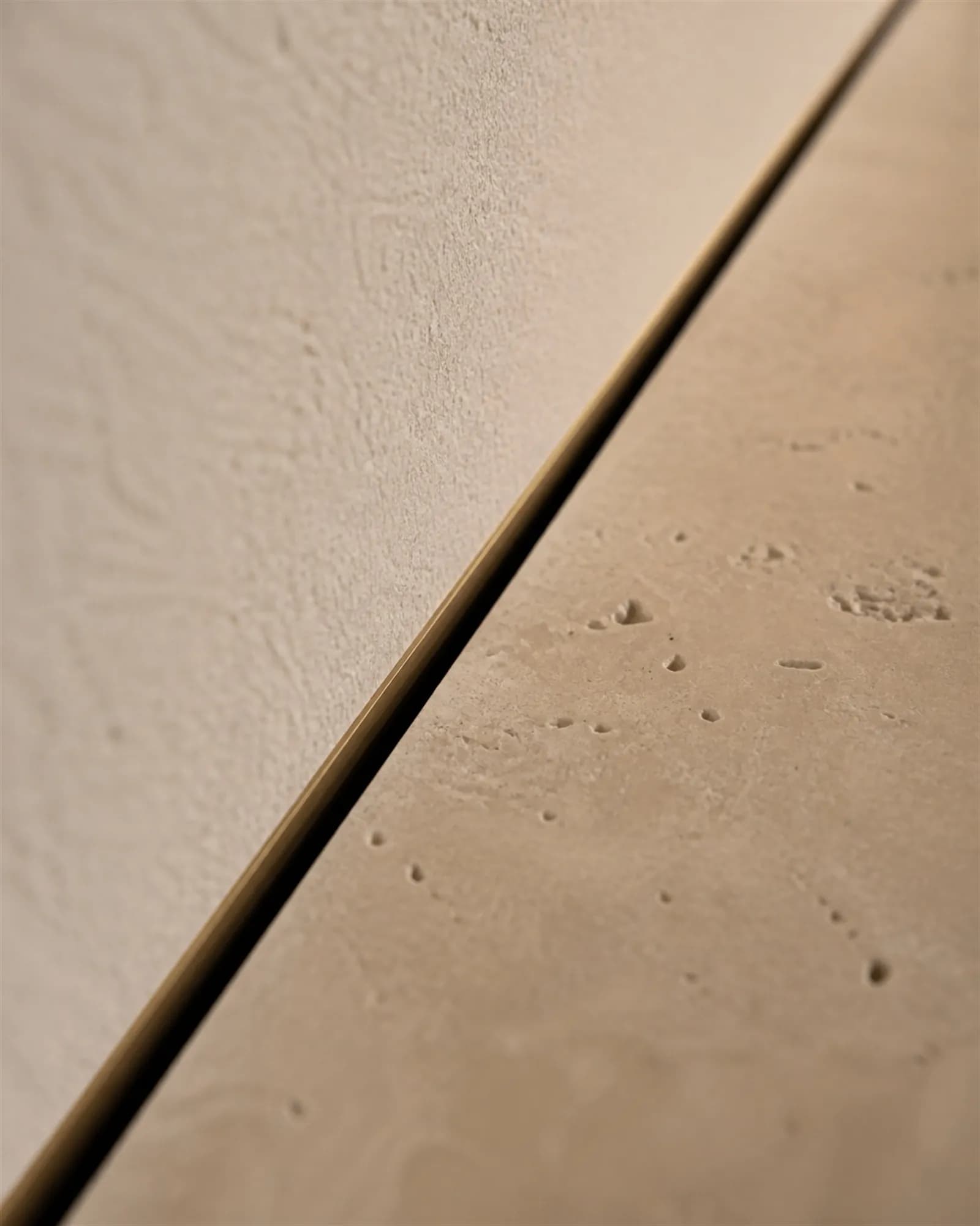 Extreme close detail of a six-millimetre bronze-lined shadow gap between plaster and travertine