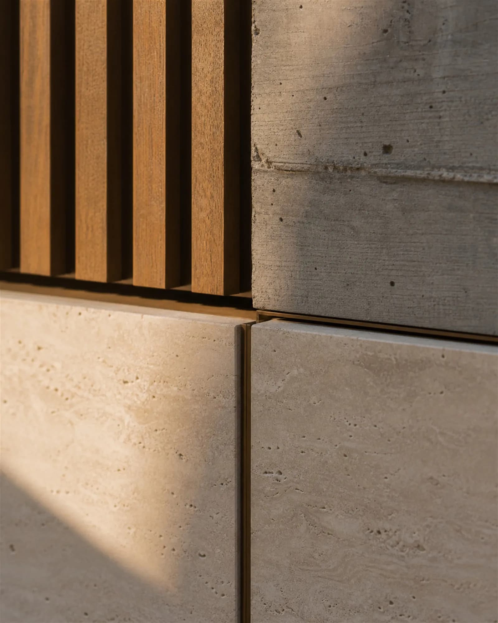 A junction where teak meets travertine and board-formed concrete, separated by precise bronze reveals
