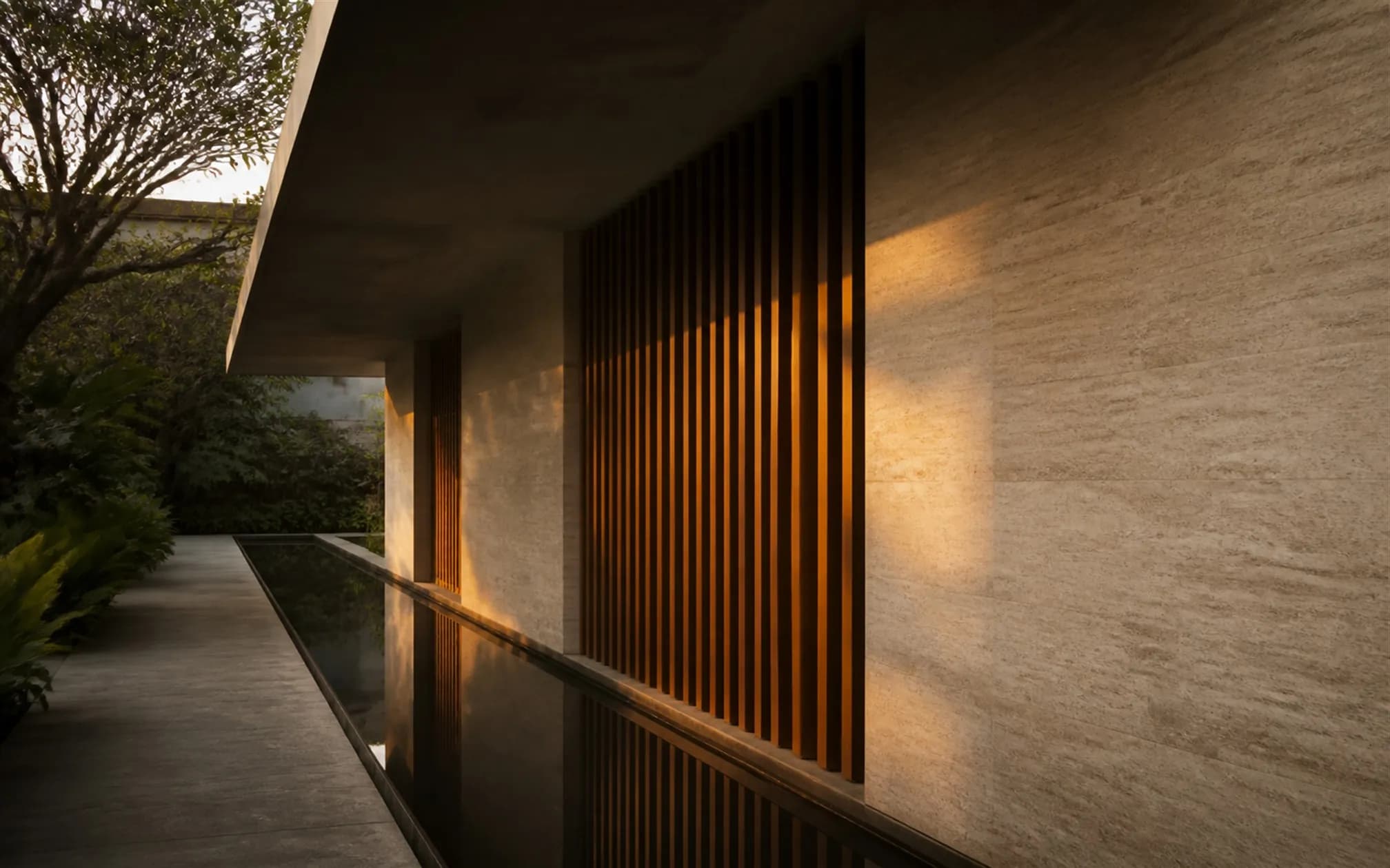 West elevation with deep concrete overhang and vertical teak baffles striping the low evening sun
