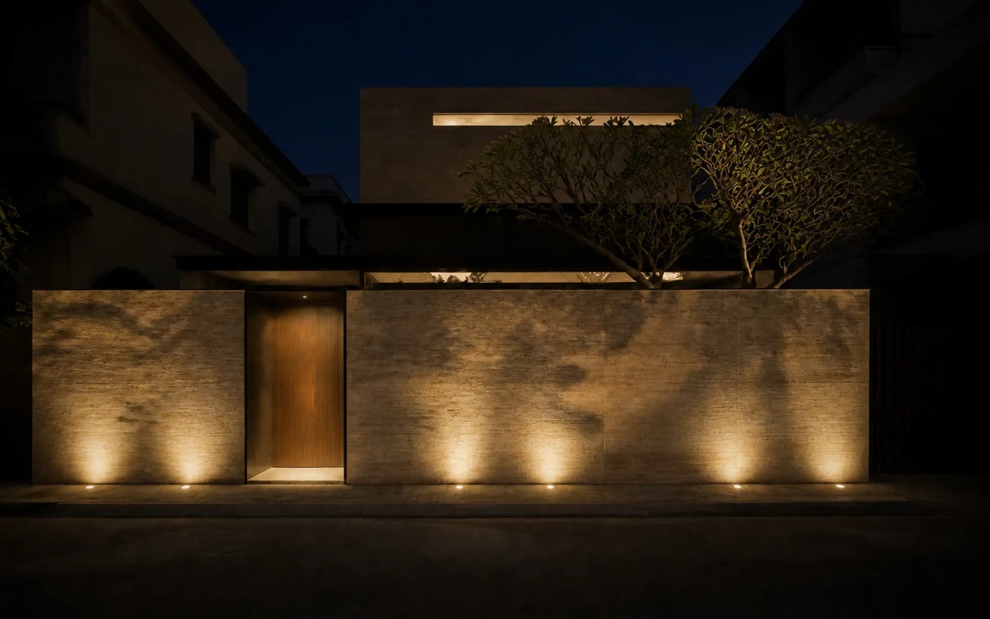 Street facade at night, travertine grazed by concealed uplighting, frangipani casting leaf shadows