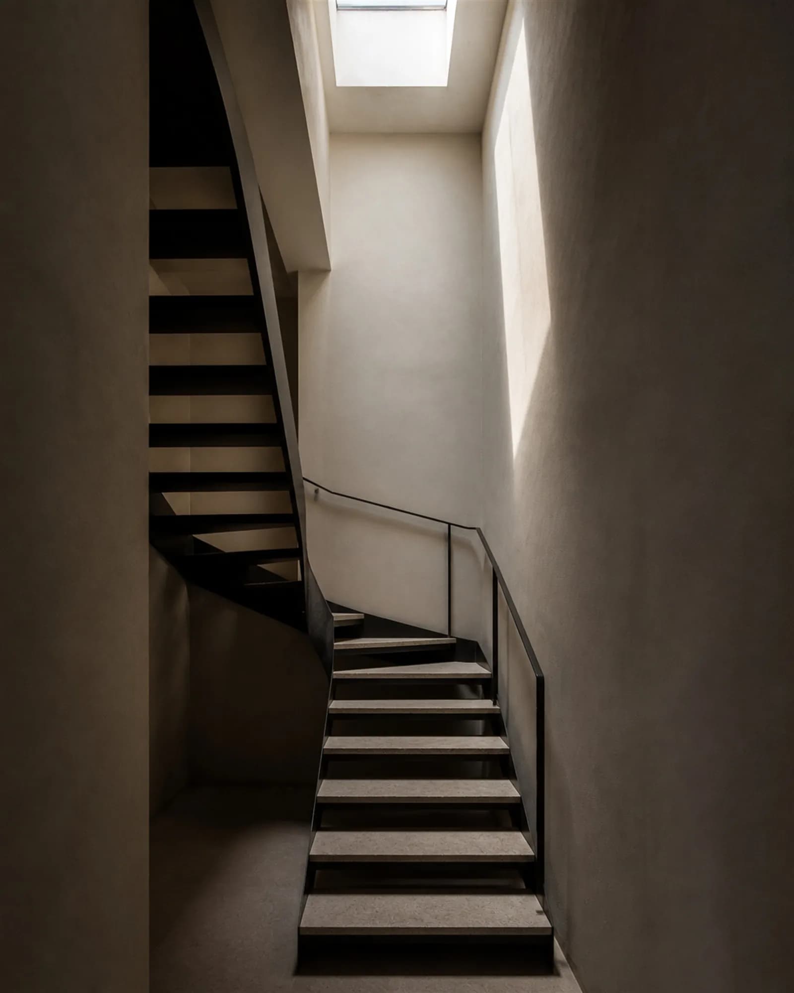 Top-lit folded steel stair winding through three levels beneath a large skylight