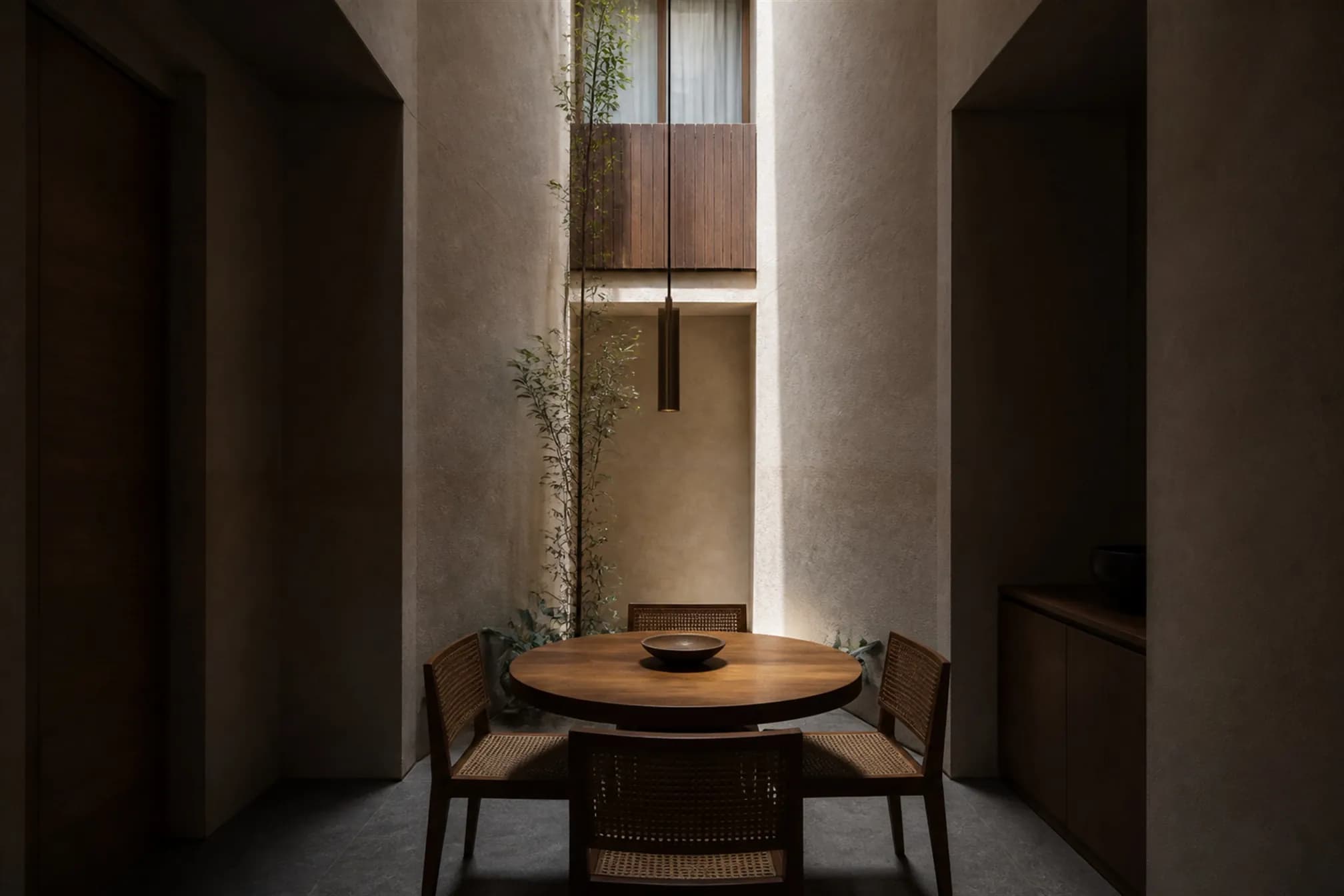 Dining space directly beneath the light slot, daylight pooling on the teak tabletop