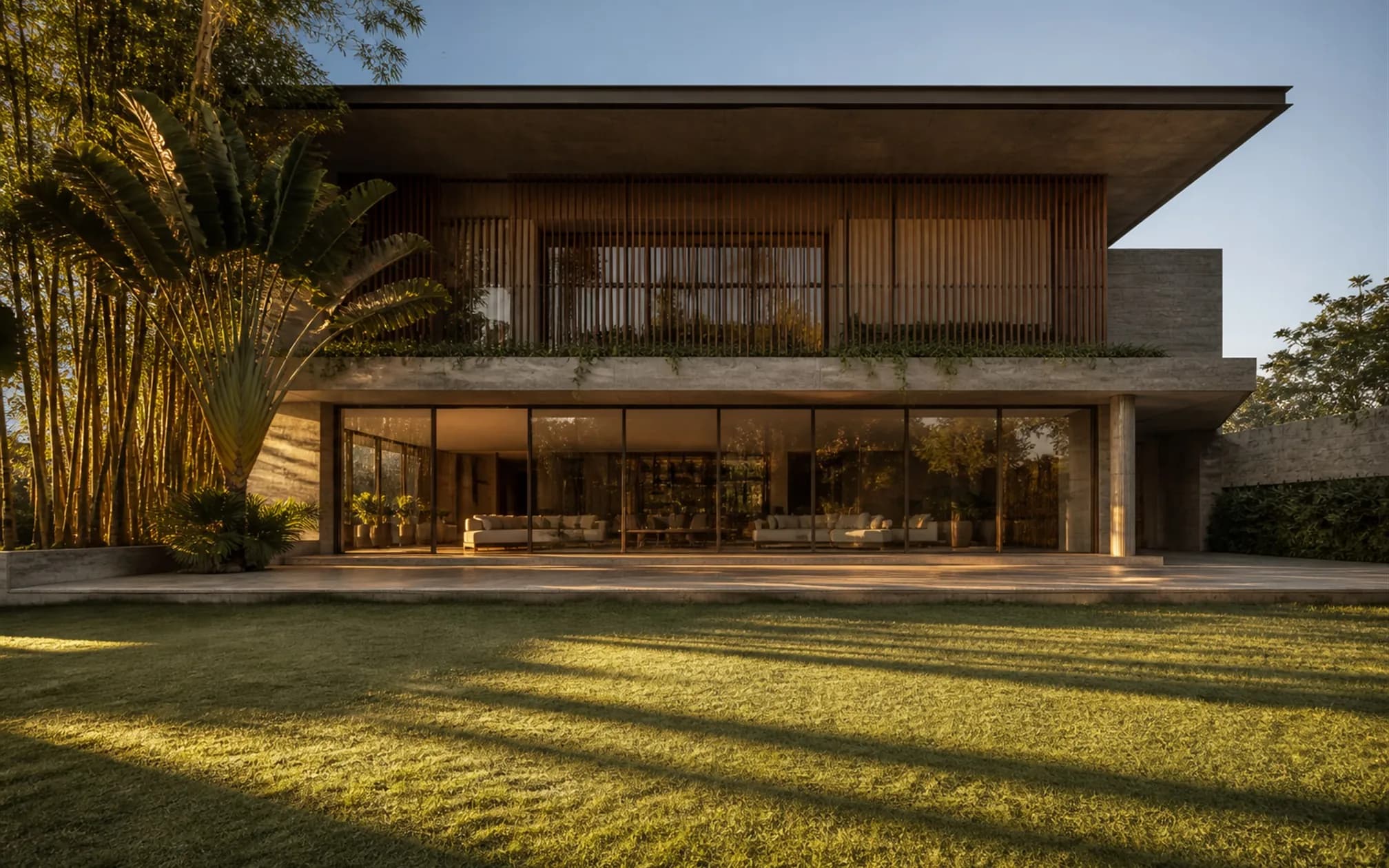 East elevation at early morning, full-height glazing opening onto a stone terrace with long shadows on dew-wet lawn
