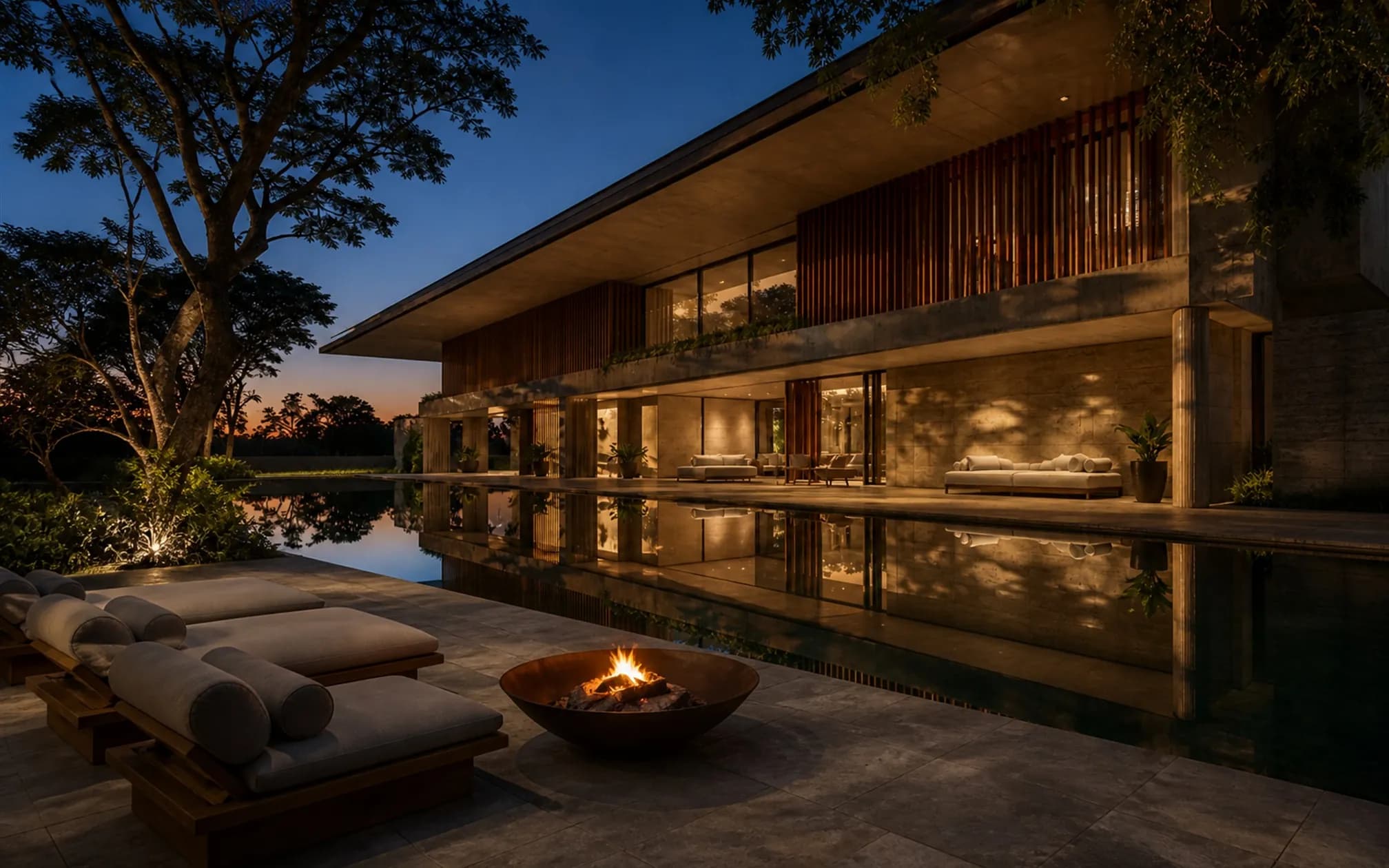 Stone terrace between the house and the reflecting pool at dusk, a lit bronze fire bowl