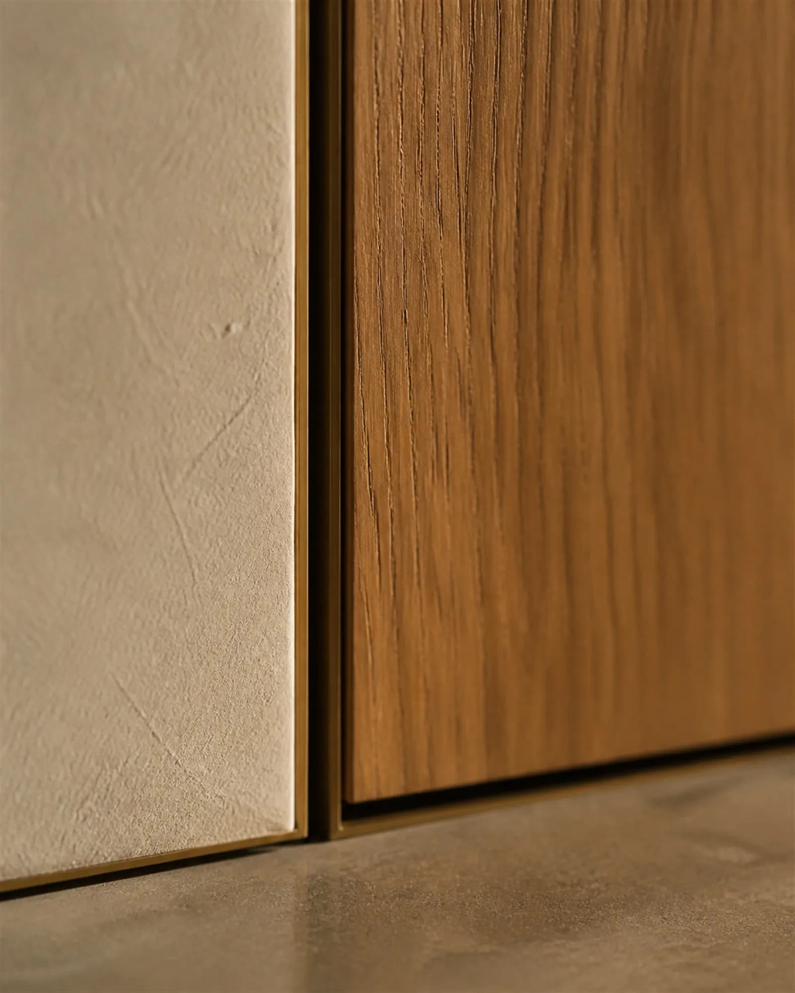 Close detail of a flush teak door panel meeting lime plaster and stone with a precise bronze-lined shadow gap
