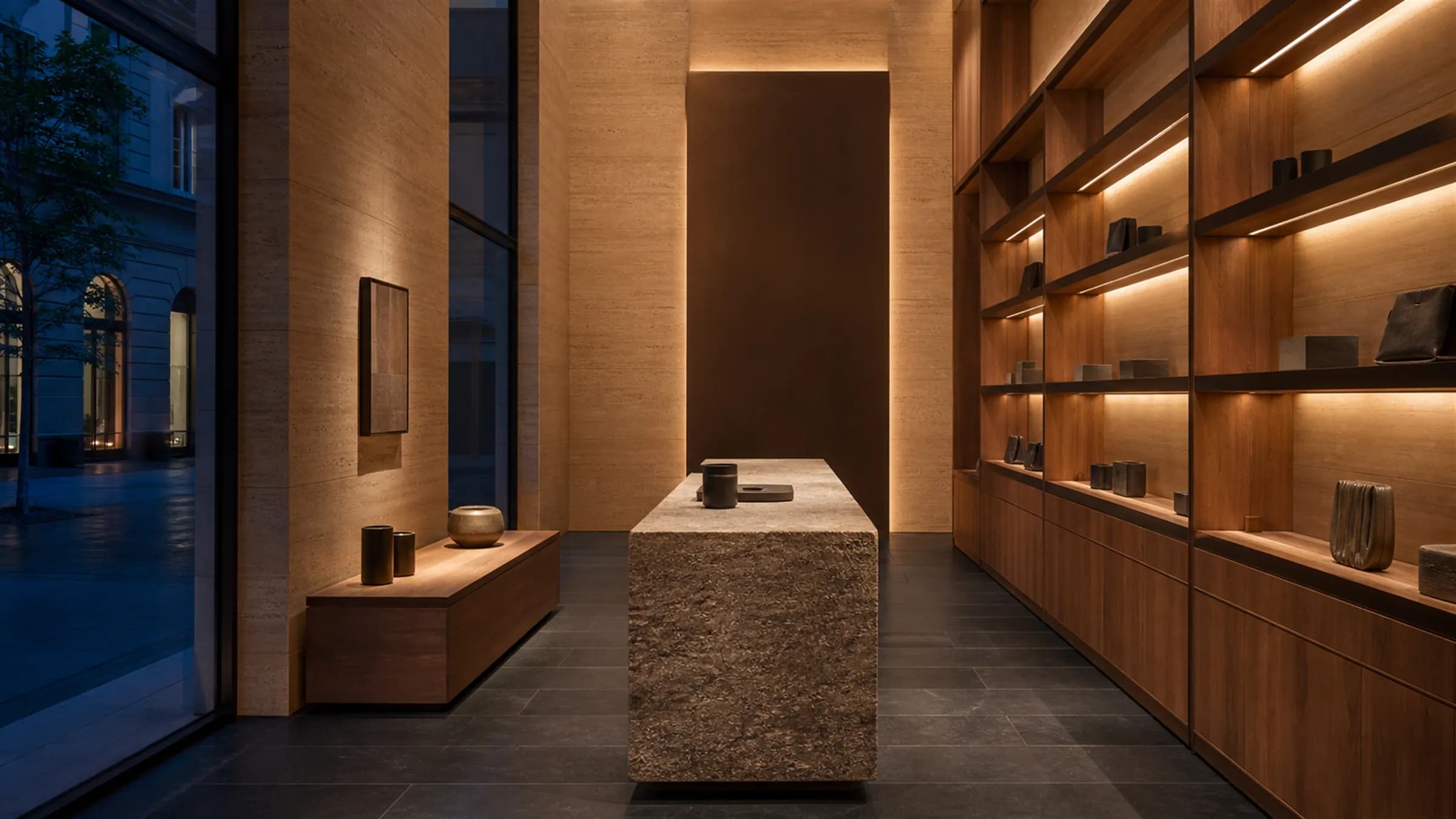 A contemporary luxury retail interior at dusk, empty and ready to trade, with teak display joinery and concealed bronze lighting