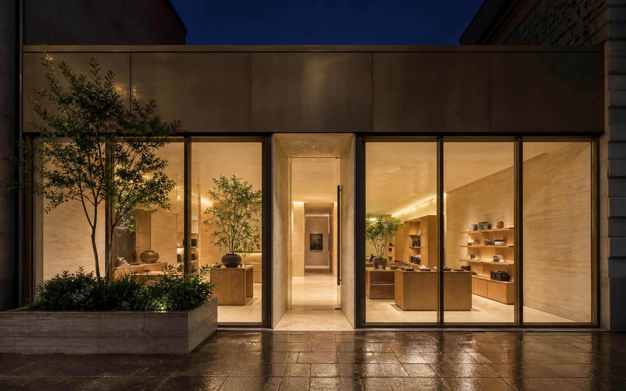 A contemporary retail shopfront at night, warmly lit through bronze-framed glazing with a blank fascia panel